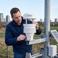 OHTS1070 Ultrasonic Weather Station installation scenario showing technician mounting the device on metal pole with solar panel in outdoor urban environment monitoring station setup